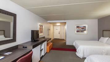 A hotel room with a desk, a television, two beds, a mirror, and a red carpet.