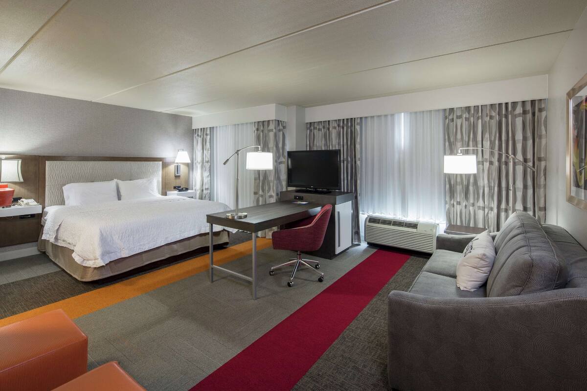 Habitación de hotel con cama, escritorio, televisor y zona de estar.