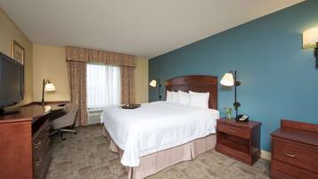 A hotel room with a large bed, a desk with a chair, a television, a nightstand with a lamp, and a dresser.