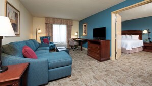 A hotel room with a blue sofa, a desk, a chair, a dresser, and a bed. - Hampton Inn & Suites Bloomington - Normal (Normal)