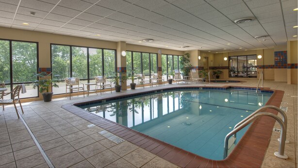 An indoor swimming pool with tiled flooring, chairs, and potted plants. - Hampton Inn & Suites Bloomington - Normal (Normal)