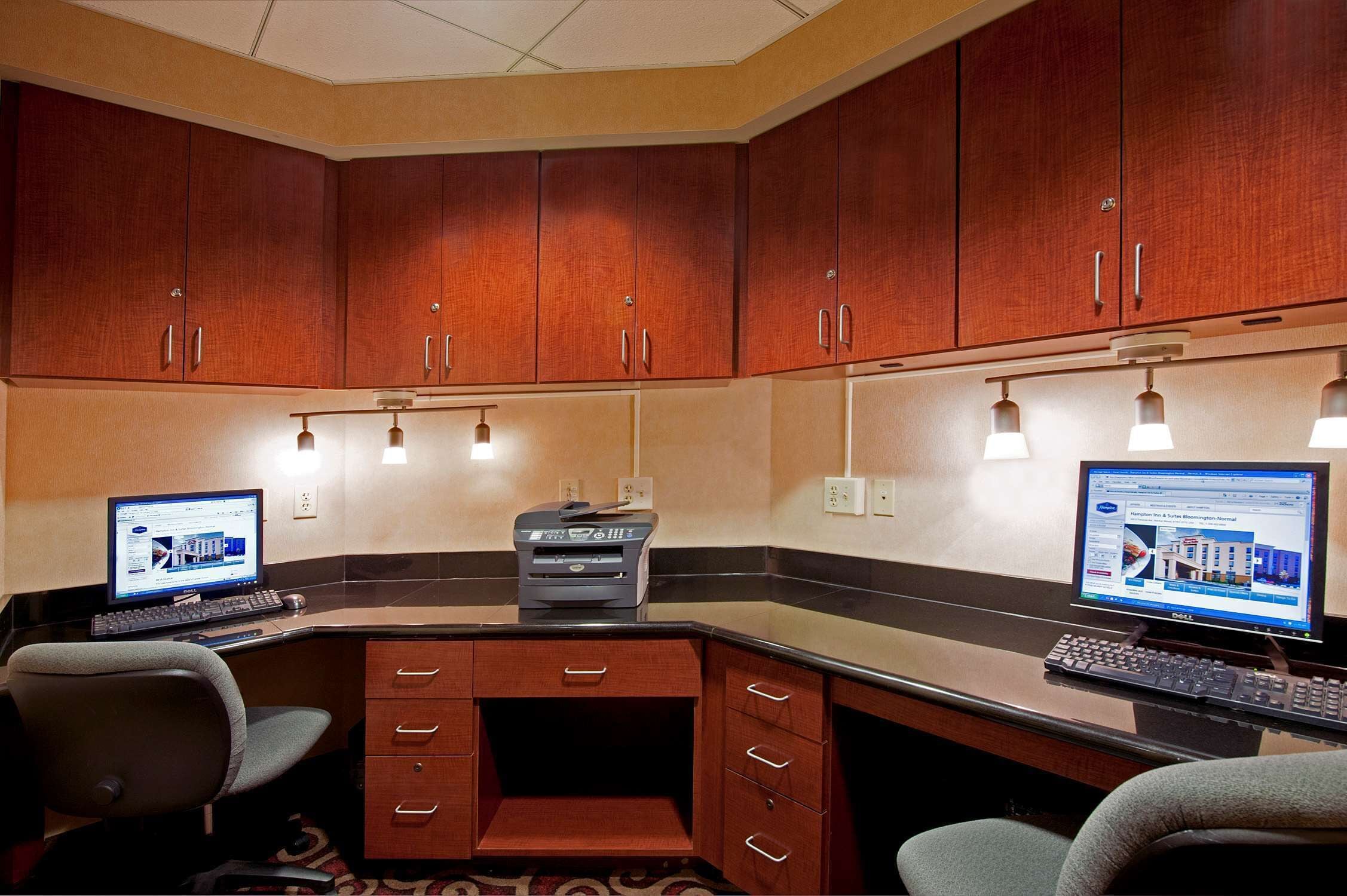A hotel office with two computer workstations, a printer, and wooden cabinets.