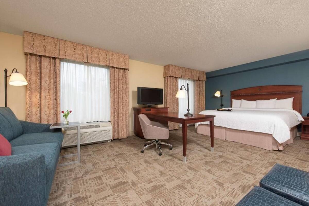 A hotel room with a bed, a desk, a chair, a television, and a lamp.