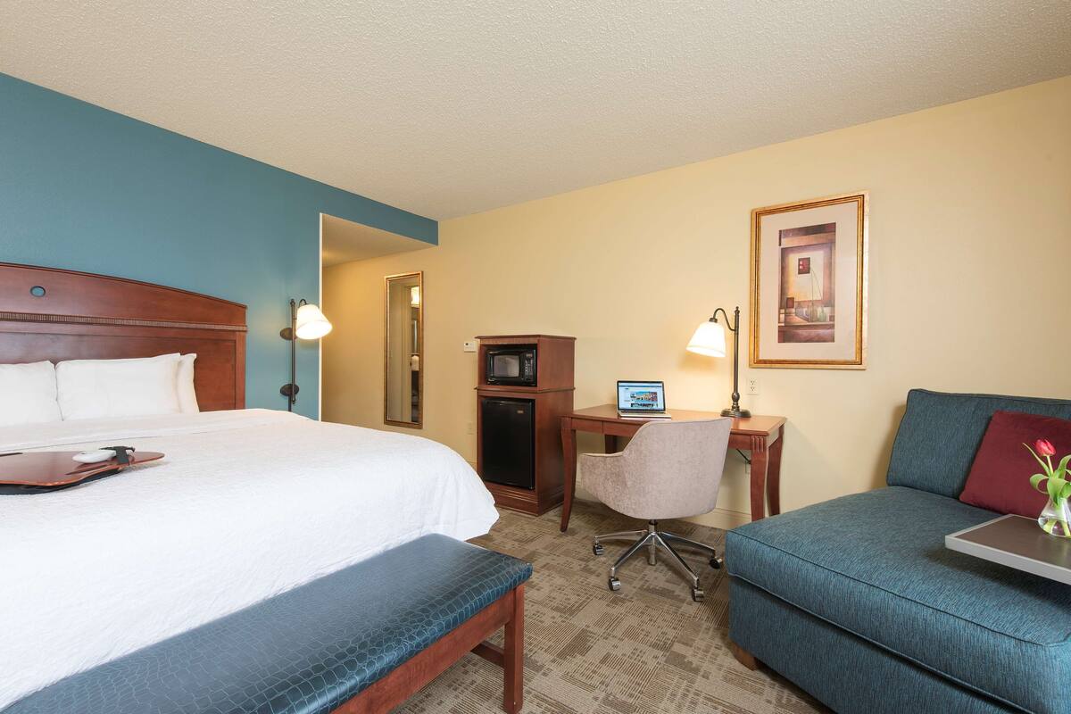A hotel room with a bed, a desk, a chair, a sofa, and a microwave.