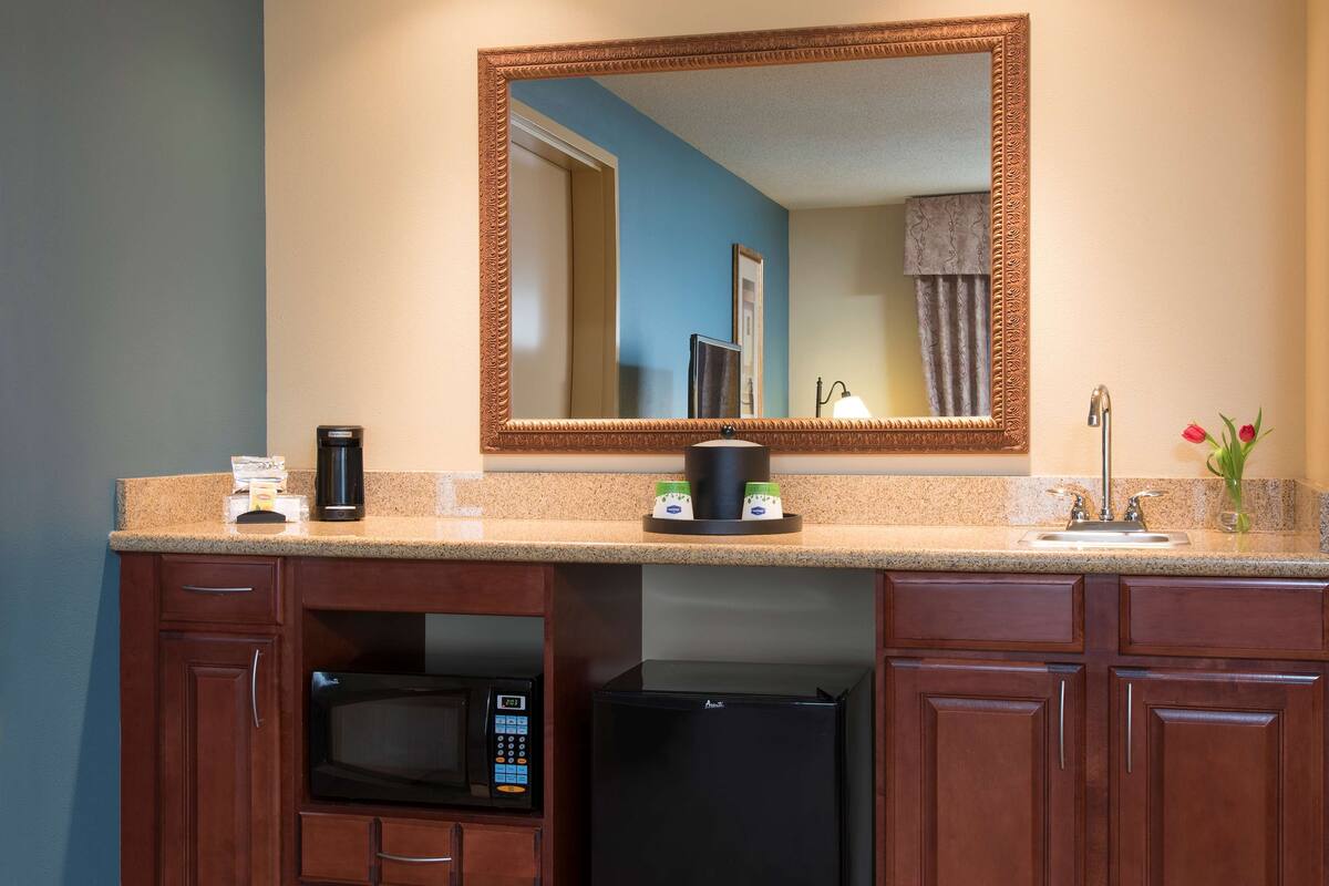 A kitchen with a microwave, refrigerator, coffee maker, and a large mirror above the countertop.