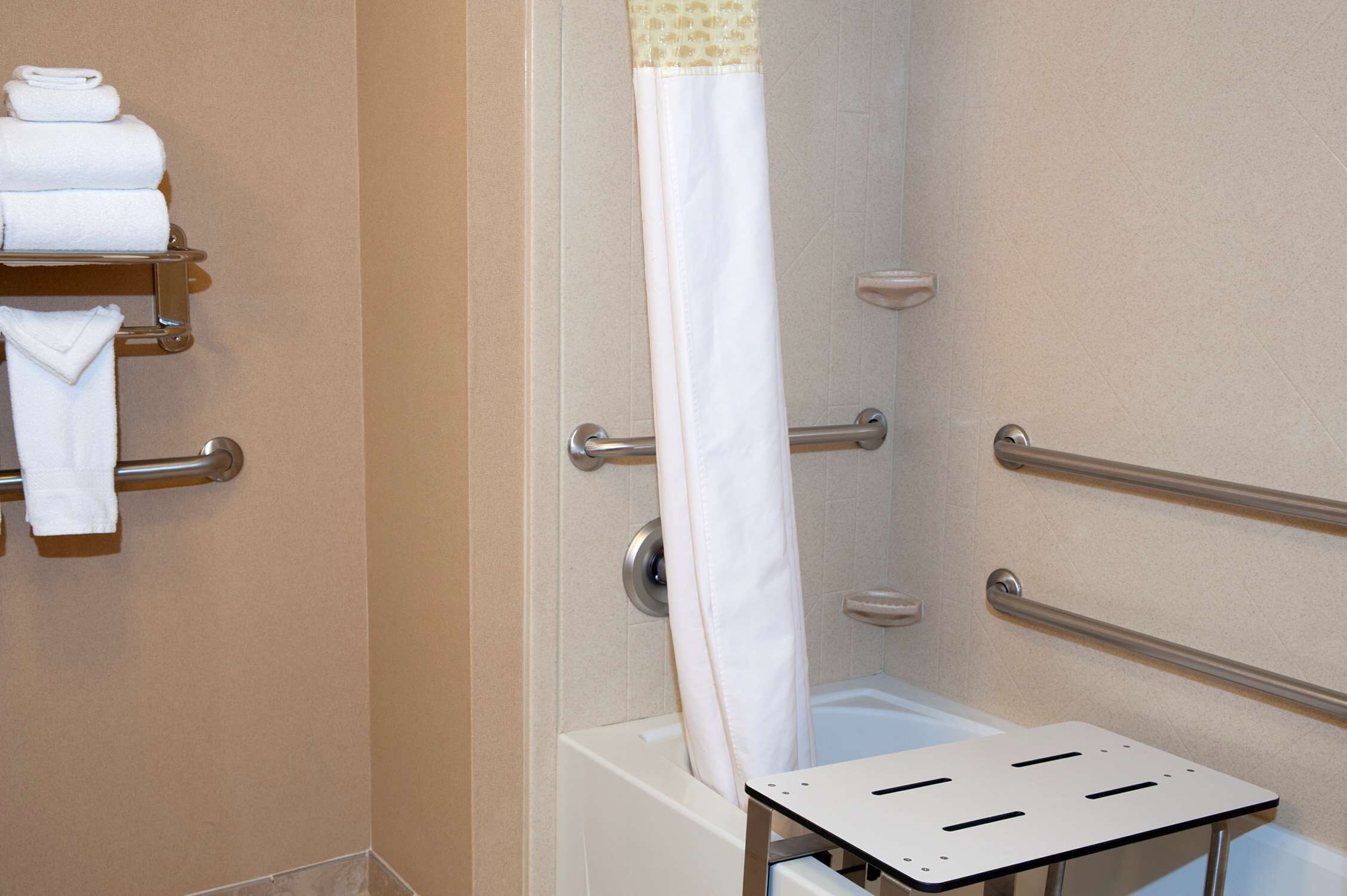 A bathroom with a bathtub, grab bars, and a towel rack with folded towels.