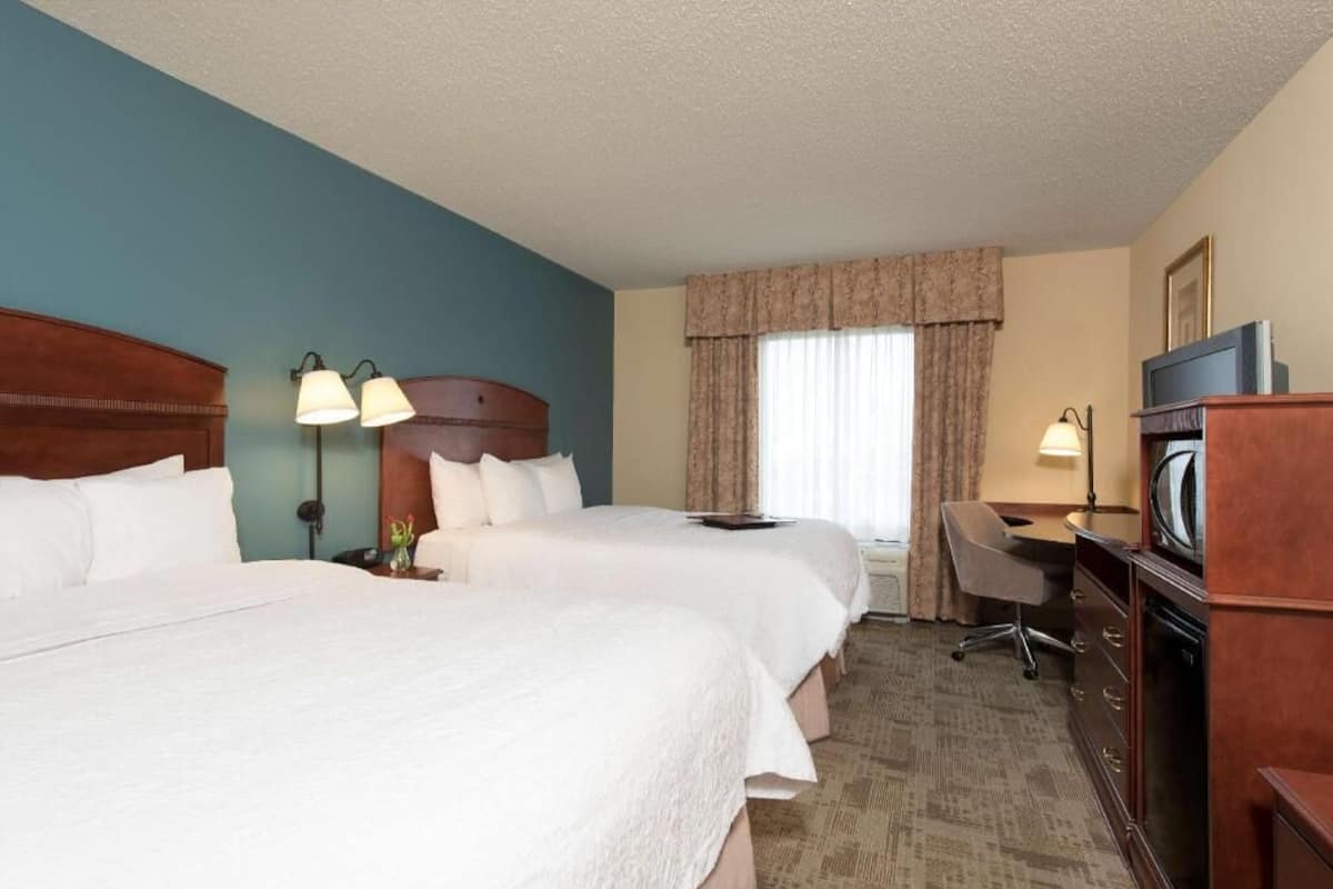 A hotel room with two beds, a desk, a chair, a television, and a window with curtains.