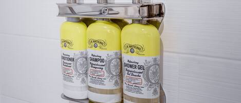 A bathroom with a chrome faucet and three bottles of J.R. Watkins products: conditioner, shampoo, and shower gel.