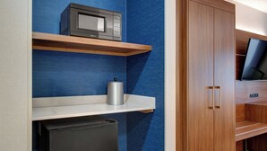 A compact kitchenette with a microwave, a small refrigerator, and a shelf with a kettle.