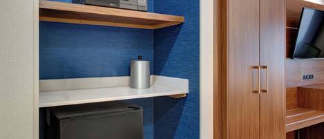 A compact kitchenette with a microwave, a small refrigerator, and a shelf with a kettle.