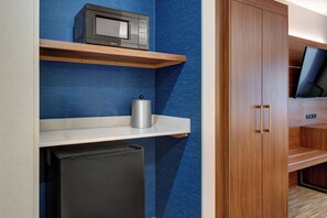 A compact kitchenette with a microwave, a small refrigerator, and a shelf with a kettle.