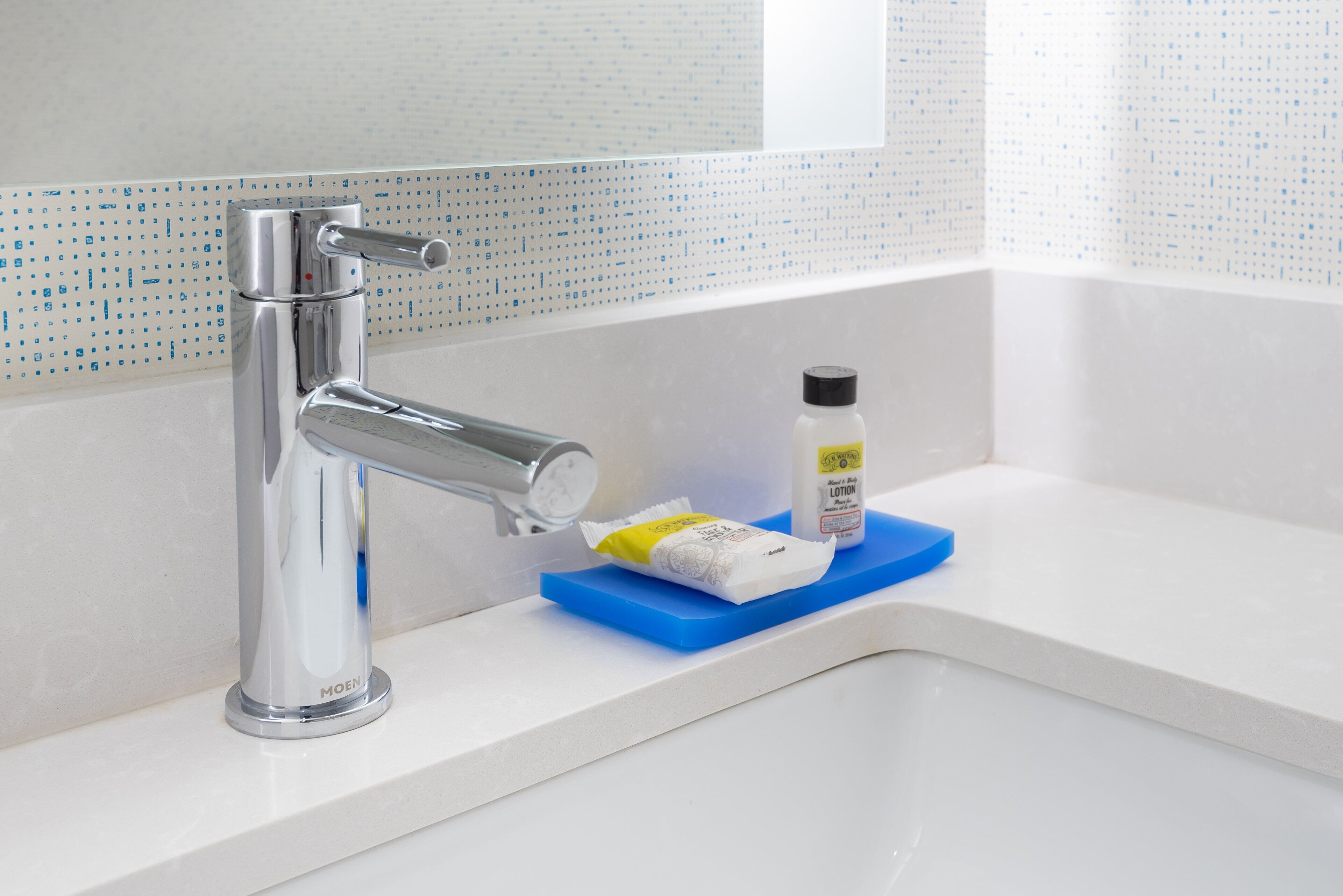 A bathroom with a chrome faucet, a white sink, and a blue soap dish.