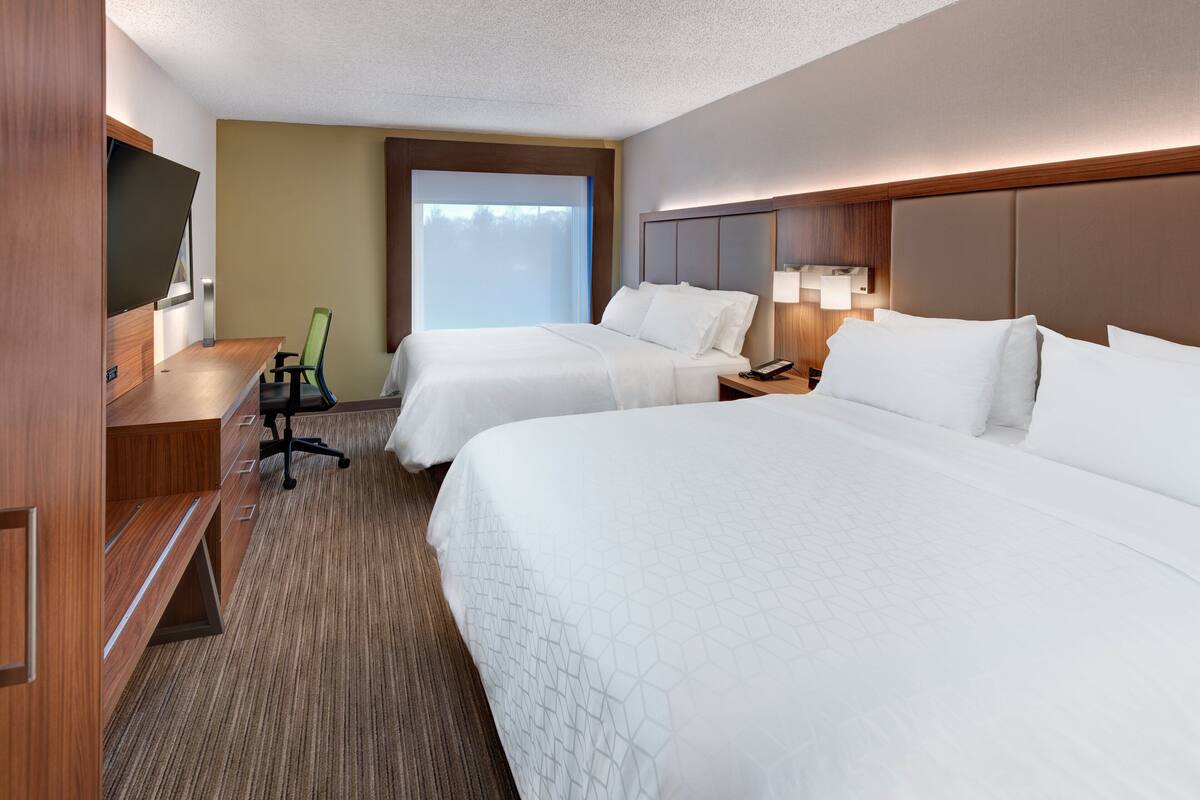 Une chambre d’hôtel avec deux lits, un bureau avec une chaise, une télévision et une fenêtre donnant sur un paysage agréable.