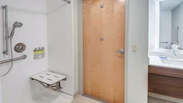 A bathroom with a wooden door, a shower with grab bars, a towel rack, and a mirror above the sink.