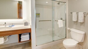 A modern bathroom with a glass-enclosed shower, a white toilet, and a vanity with a mirror and towel rack.
