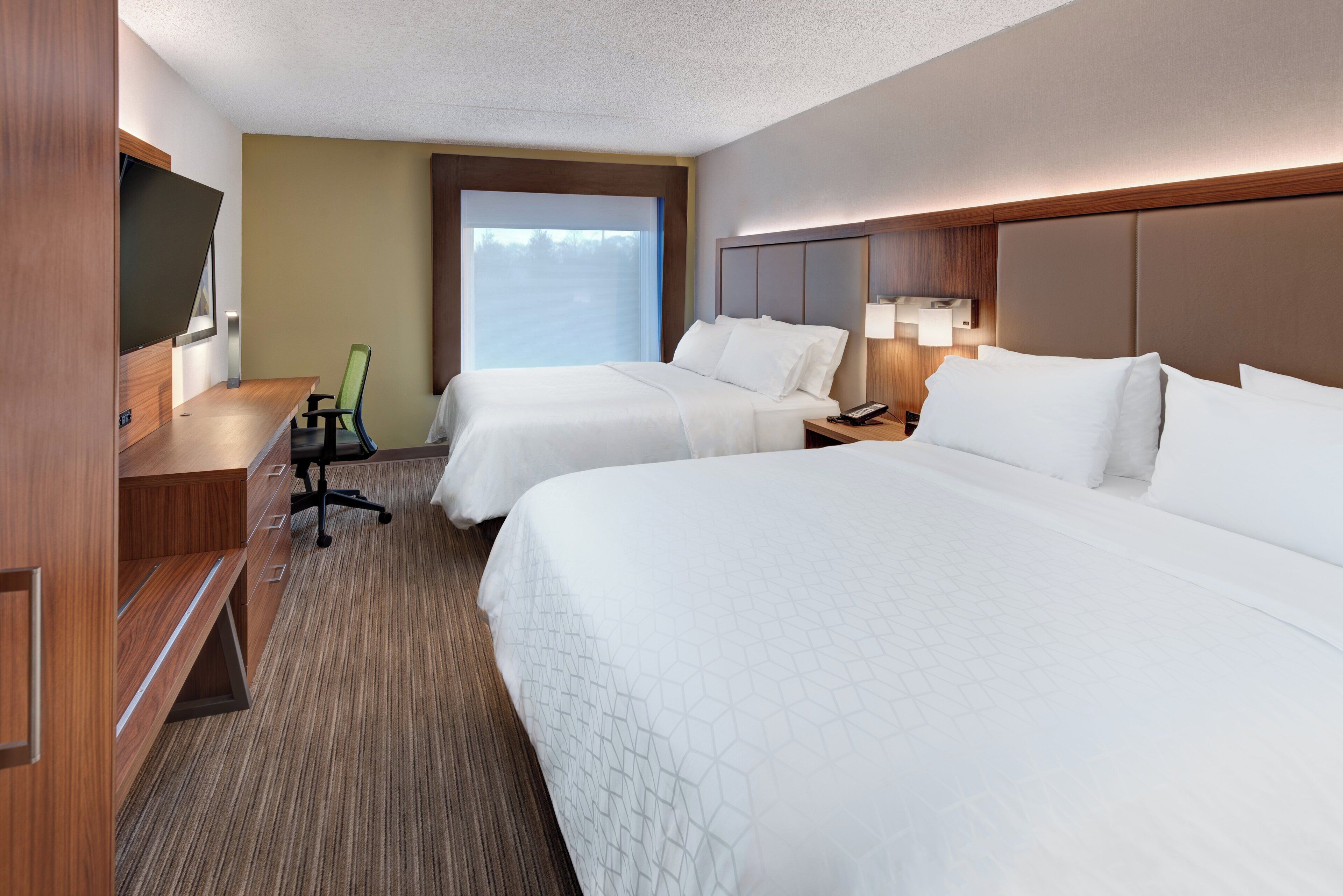 A hotel room with two beds, a desk, a chair, a TV, and a window.