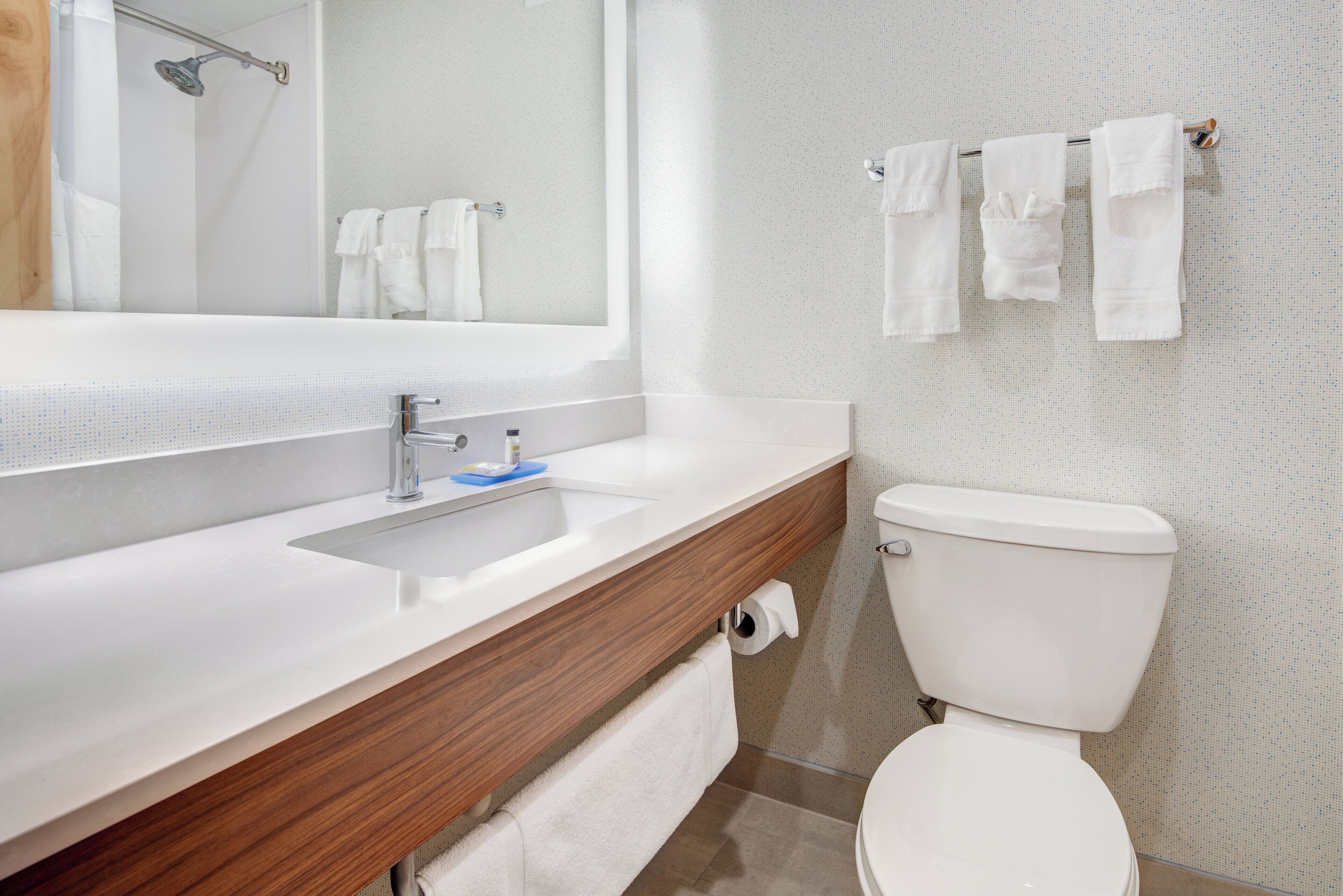 A modern bathroom with a white sink, wooden vanity, a toilet, and a shower area.