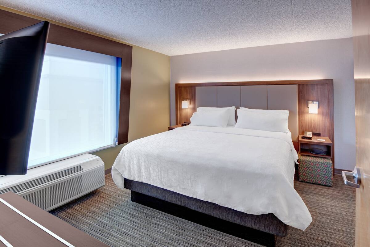 Une chambre d’hôtel avec un grand lit, un téléviseur à écran plat, un radiateur et une fenêtre équipée de stores.