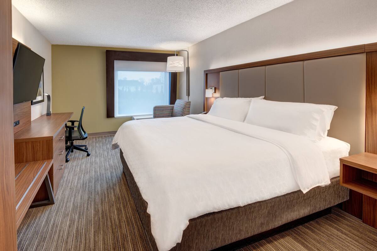 Une chambre d’hôtel avec un grand lit, un bureau avec une chaise, une télévision et une fenêtre donnant sur un beau paysage.