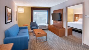 A hotel room with a blue sofa, a wooden coffee table, a TV, a desk, and a bed.