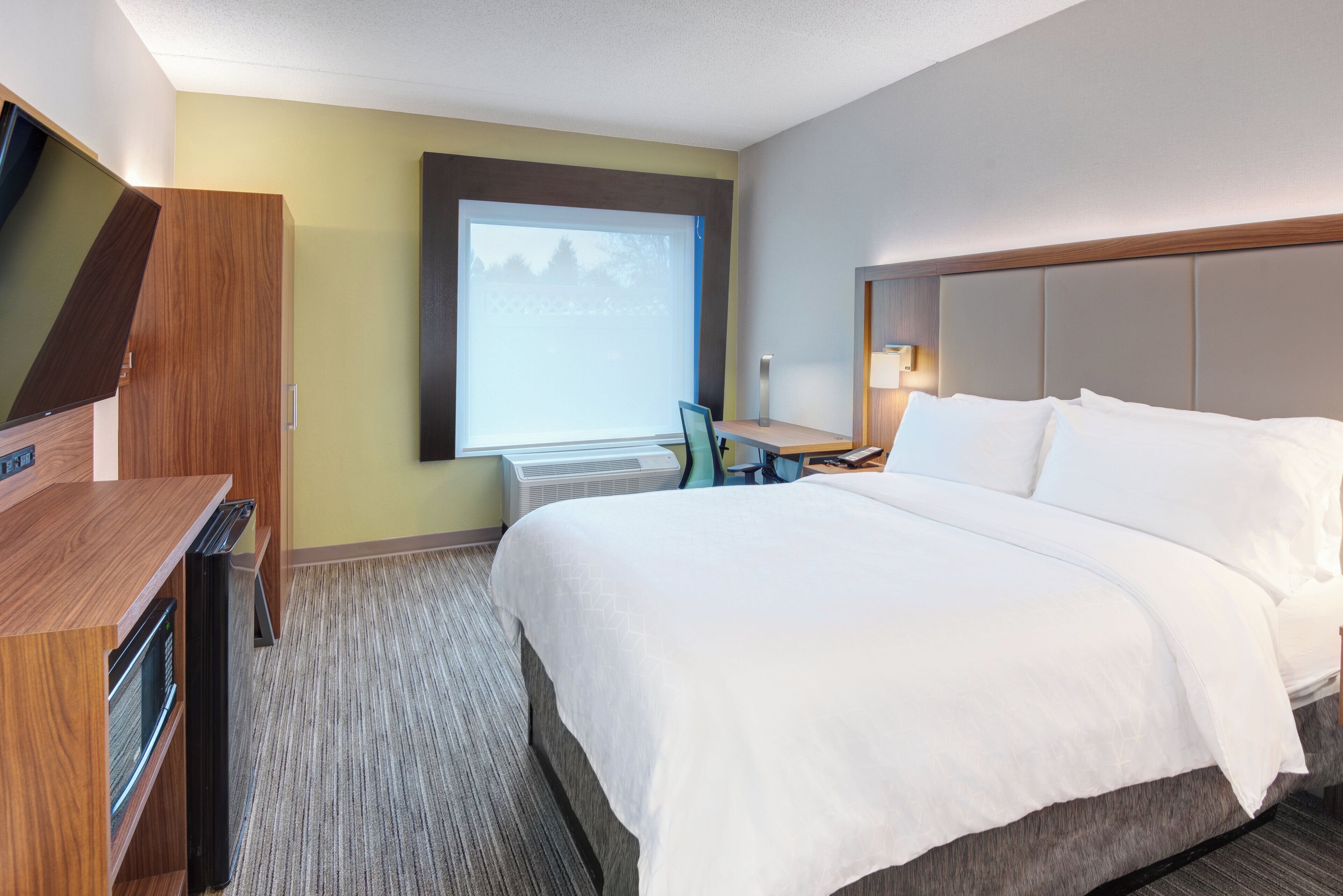 A hotel room with a bed, a desk, a chair, a TV, and a window.