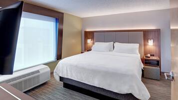 Una habitación de hotel con una cama grande, televisión de pantalla plana, aire acondicionado y una ventana con persianas.