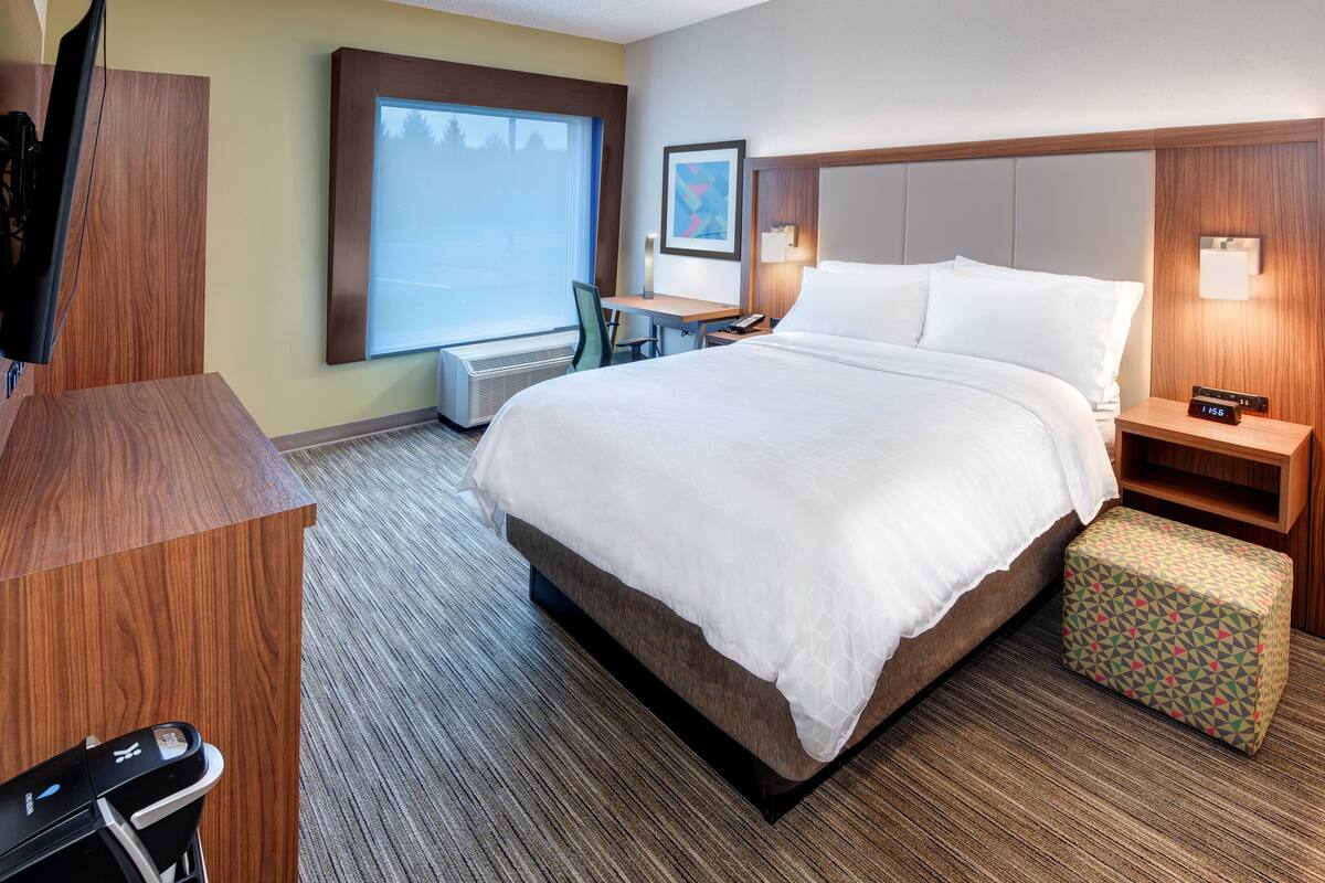 Une chambre d’hôtel avec un grand lit, un bureau, une chaise, une télévision et une petite table avec une horloge.