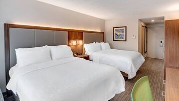 A hotel room with two beds, a wooden headboard, bedside lamps, a green chair, and a wooden wardrobe.