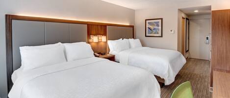 Habitación de hotel con dos camas, cabecero de madera, lámparas de noche, una silla verde y un armario de madera.