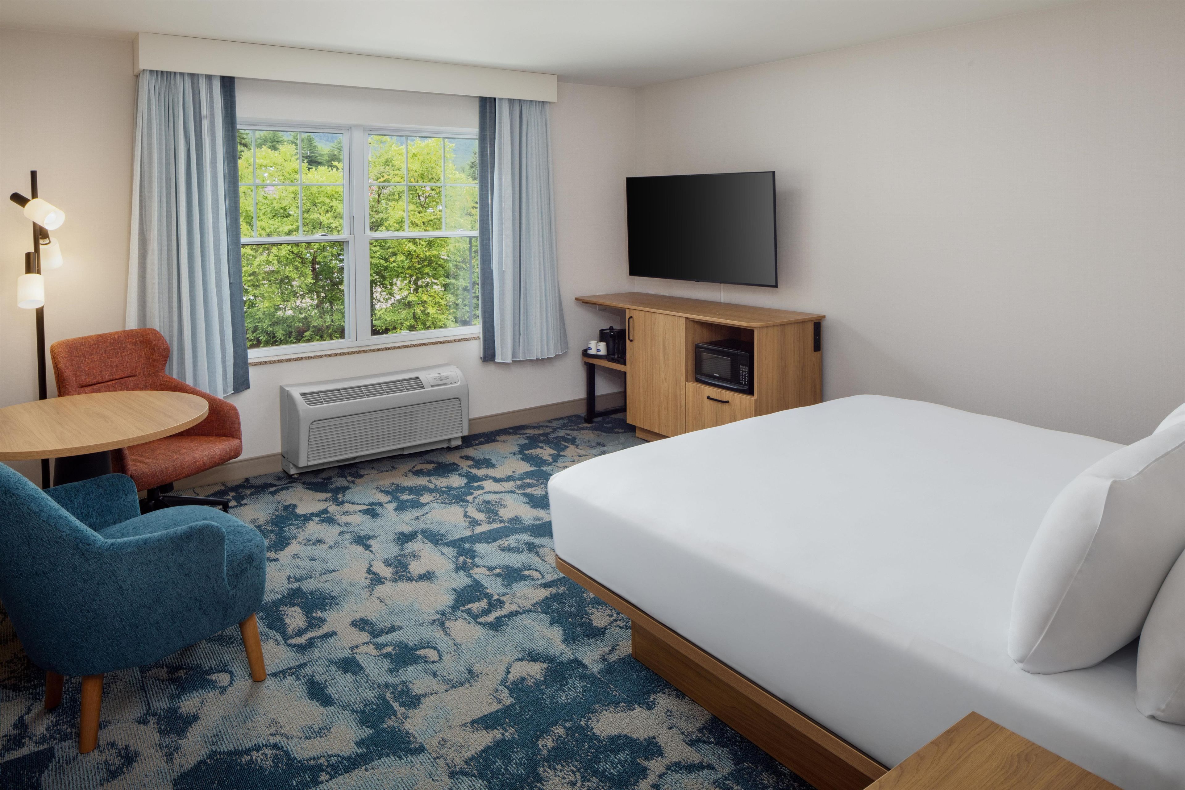 A hotel room with a bed, a desk, a chair, a TV, and a window with curtains.