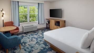 A hotel room with a bed, a desk, a chair, a TV, and a window with curtains.