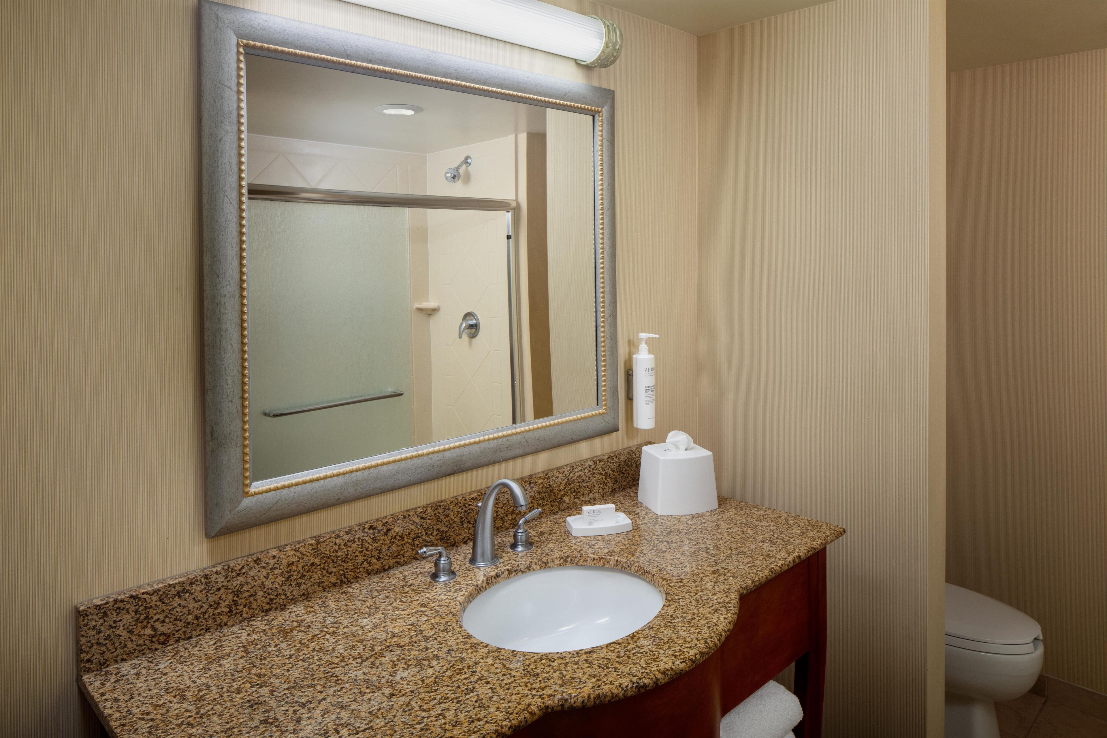 A bathroom with a granite countertop, a sink, a mirror, a towel rack, and a toilet.