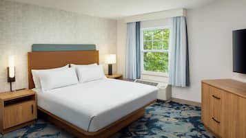 A hotel room with a large bed, bedside lamps, a window with curtains, a flat-screen TV, and a wooden dresser.