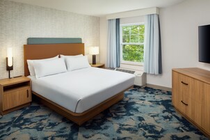 A hotel room with a large bed, bedside lamps, a window with curtains, a flat-screen TV, and a wooden dresser.