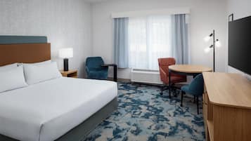 Habitación de hotel con una cama grande, un escritorio, dos sillas, un calentador y una ventana con cortinas.