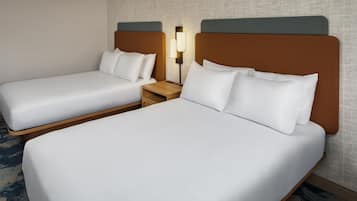 A hotel room with two single beds, a nightstand with a lamp, and a patterned carpet.