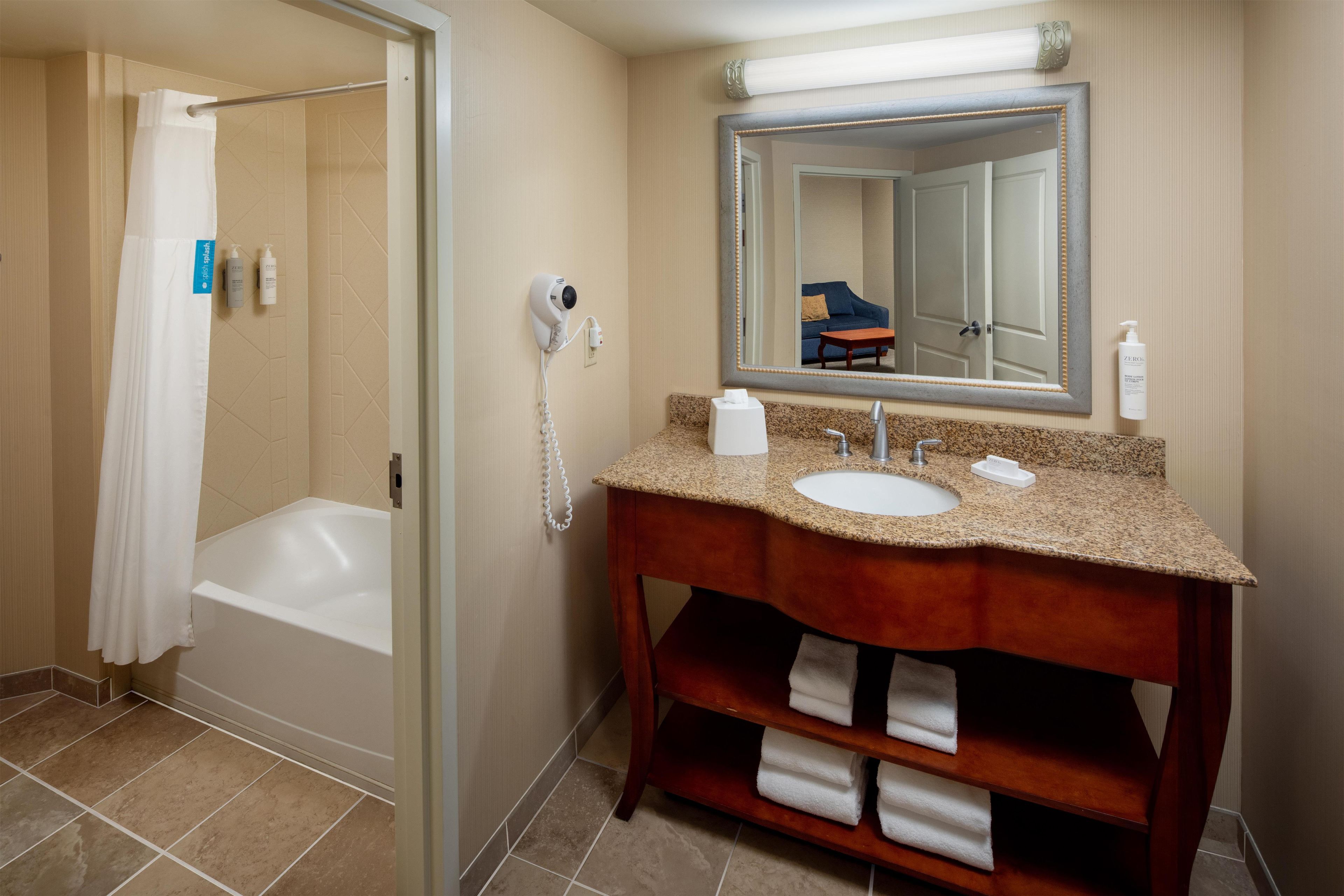 A bathroom with a bathtub, a sink, a vanity with a mirror, and a towel rack.