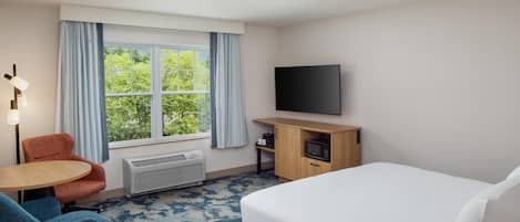 A hotel room with a bed, a desk, a chair, a TV, and a window with curtains.