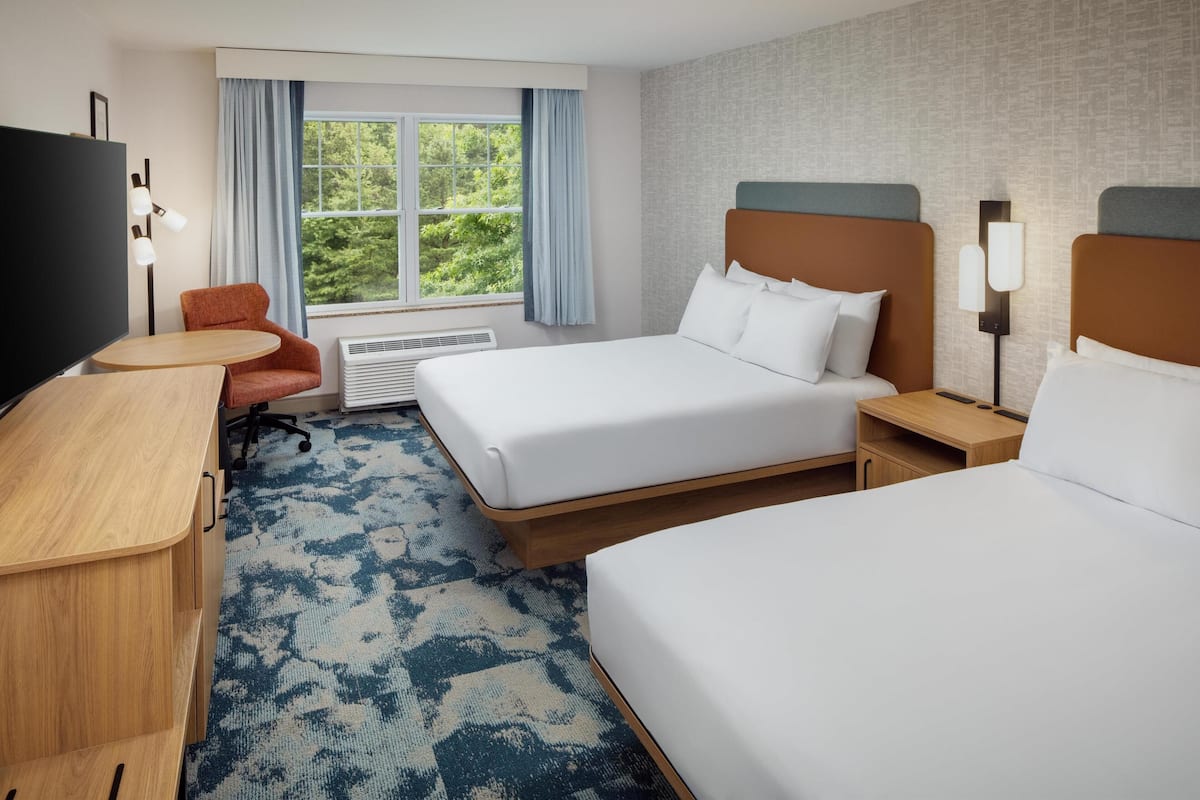 A hotel room with a bed, a desk, a chair, a TV, and a window with curtains.
