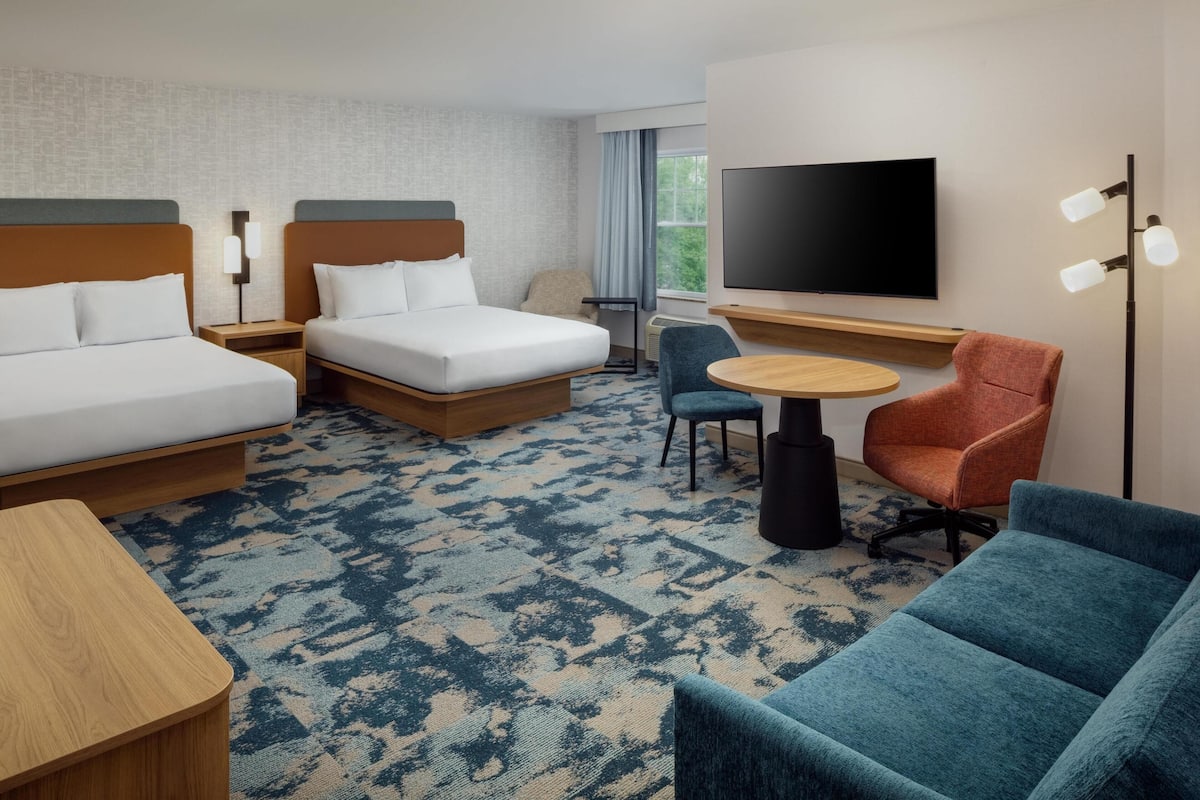 A hotel room with two beds, a TV, a desk, and a chair.