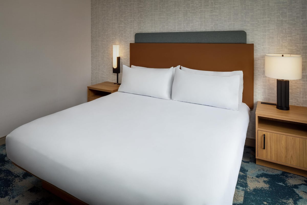 A neatly made bed with white linens, a wooden headboard, and two bedside tables with lamps.