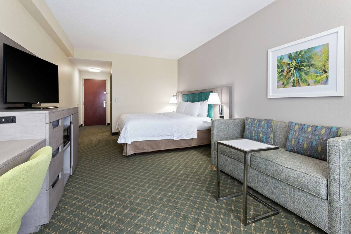 Habitación de hotel con cama, sofá, televisión, escritorio y un cuadro en la pared.