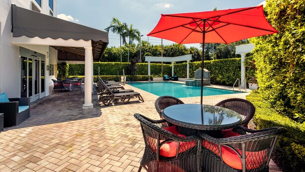Zona de piscina con sillas de mimbre, una mesa y un paraguas rojo.