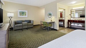 Una habitación de hotel con cama, escritorio, silla, sofá, televisor, lámpara, espejo y un cuadro en la pared.