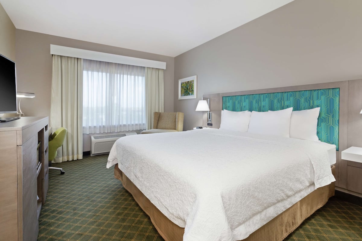 Una habitación de hotel con una cama grande, un escritorio con lámpara, una silla y un televisor.