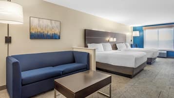 Una habitación de hotel con un sofá azul, una mesita, dos camas, un cuadro y un ventanal grande.