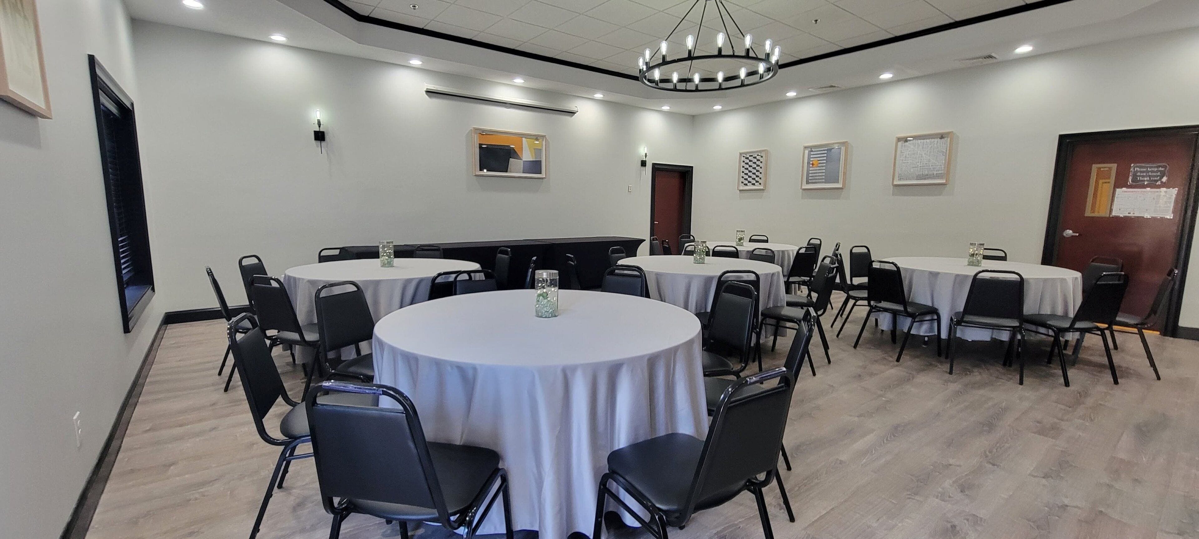 A conference room with round tables, black chairs, and white tablecloths.