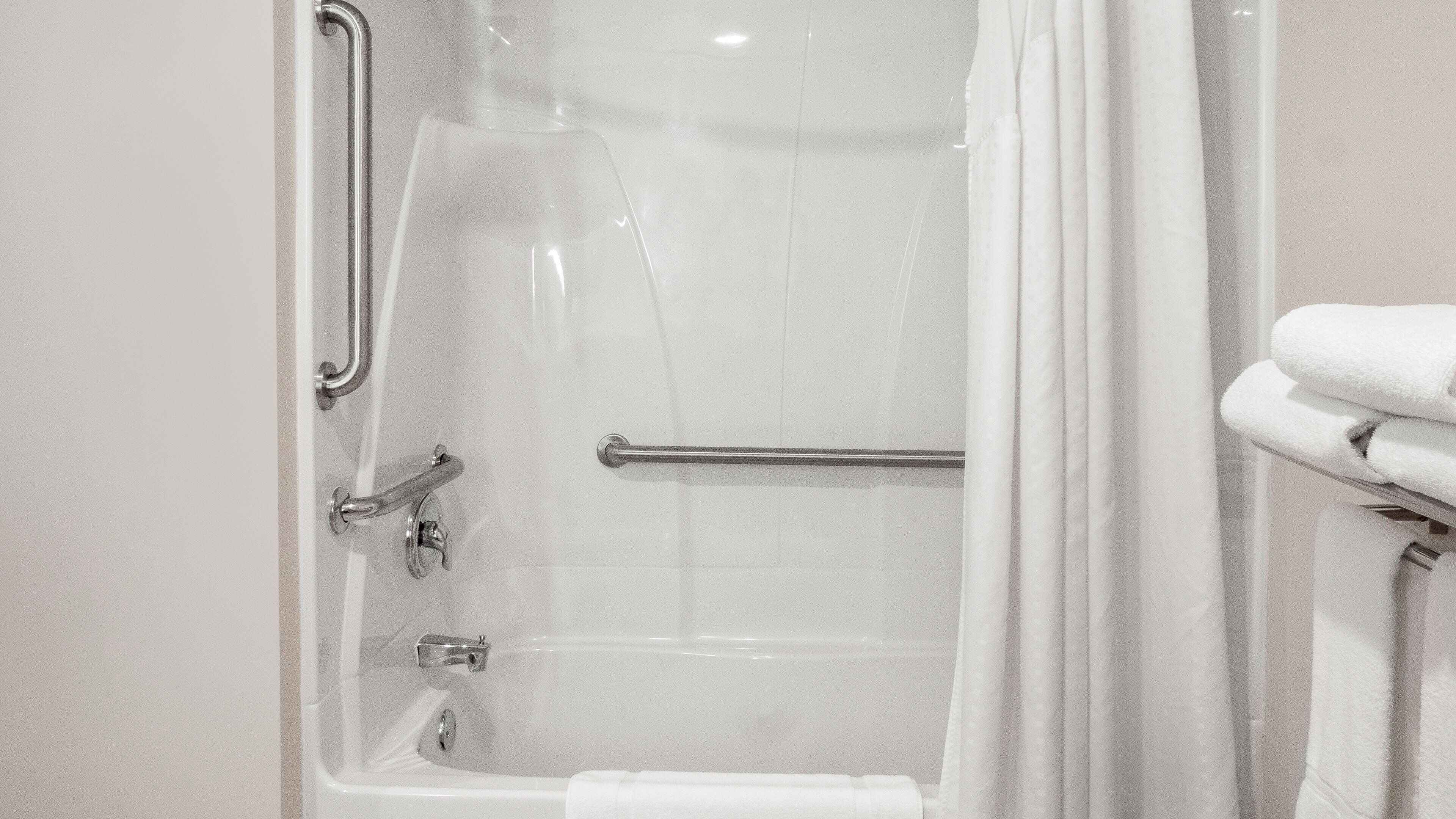 A bathroom with a bathtub, a shower curtain, a grab bar, and a towel rack with towels.
