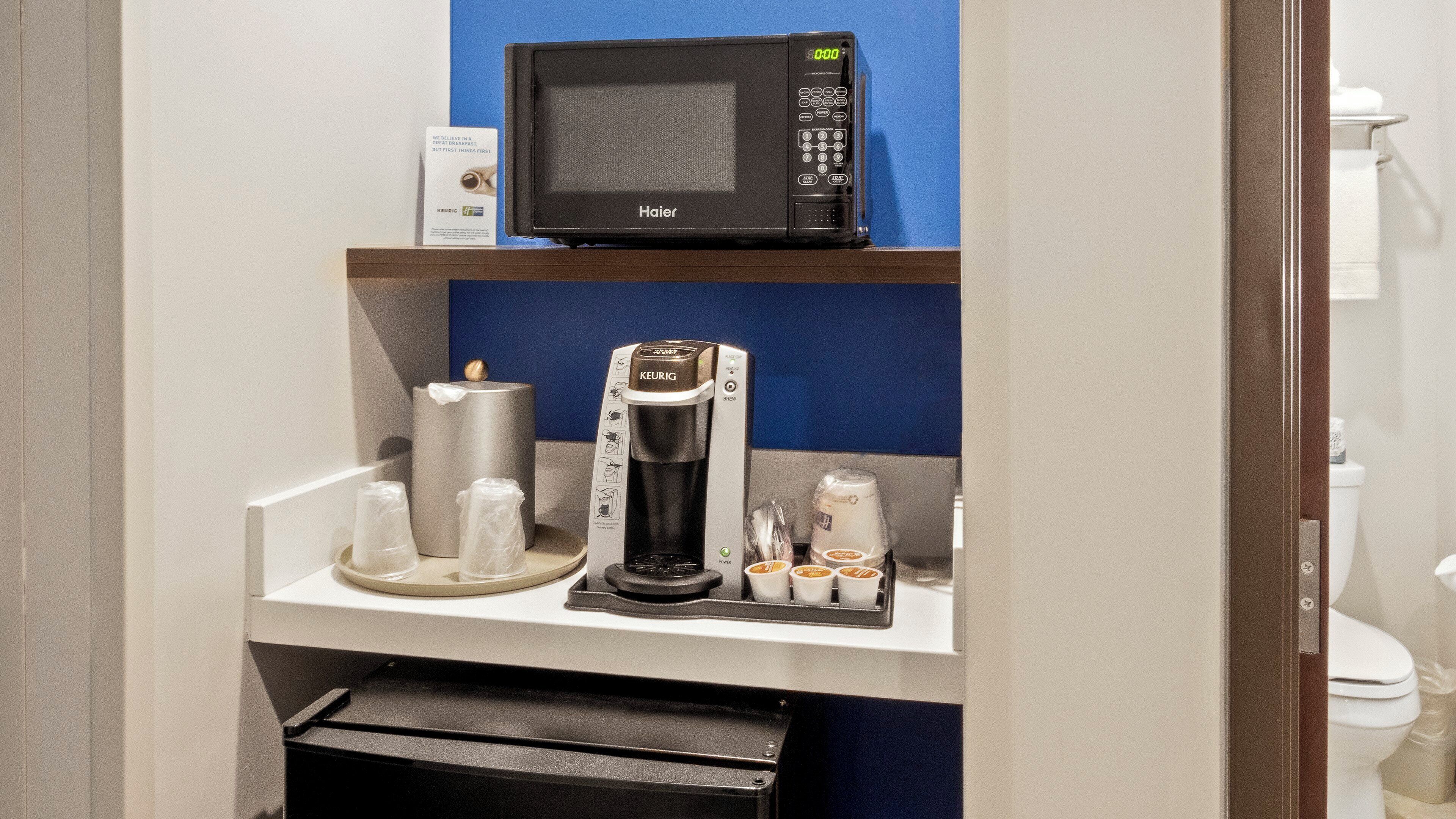 Una kitchenette equipada con microondas, cafetera y cápsulas de café.
