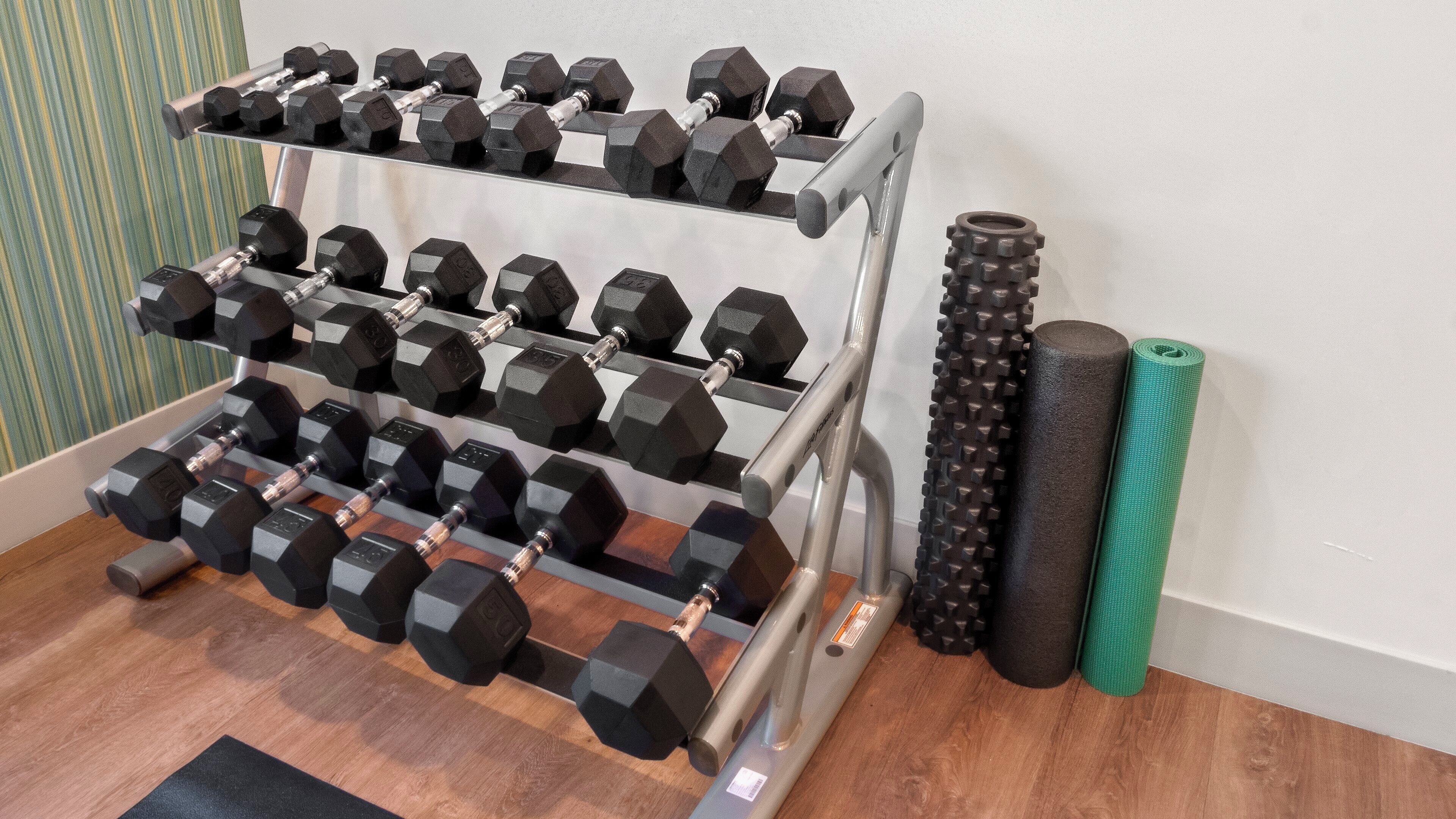 Un gimnasio en casa con un soporte de mancuernas escalonado, una colchoneta de yoga y un rodillo de espuma.
